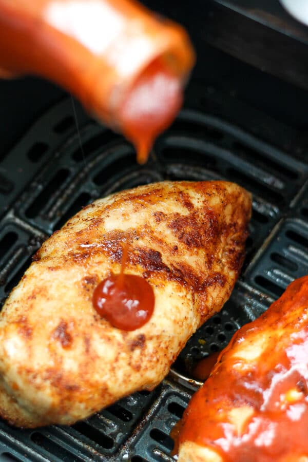 pouring barbecue sauce onto seasoned and cooked chicken breasts