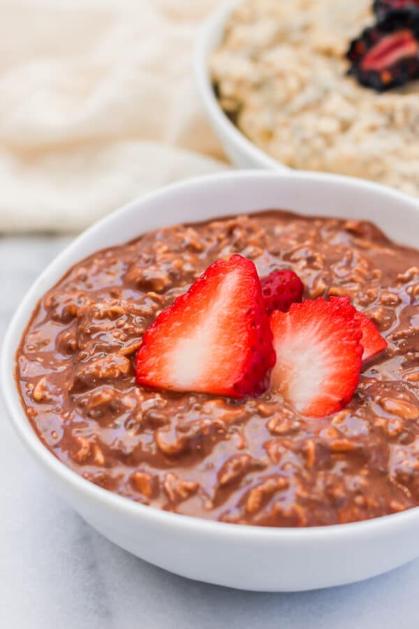 A close up of a bowl of fudgy chocolate protein overnight oats topped with sliced strawberries.