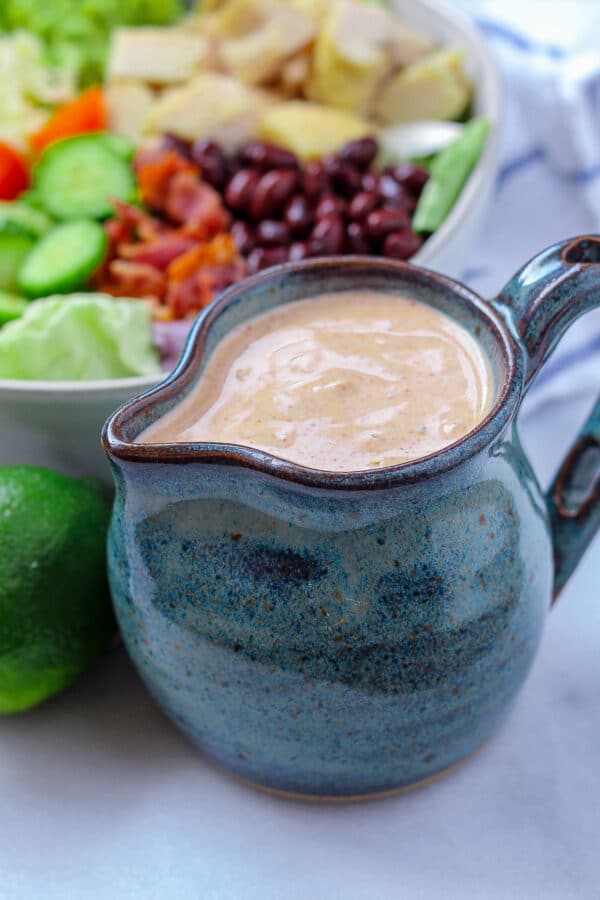 a small blue ceramic carafe filled with creamy southwest salad dressing, with a southwest avocado chicken salad in the background.