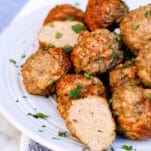 a plate of crispy meatballs garnished with fresh parsley, with one meatball cut open to exhibit juicy interior