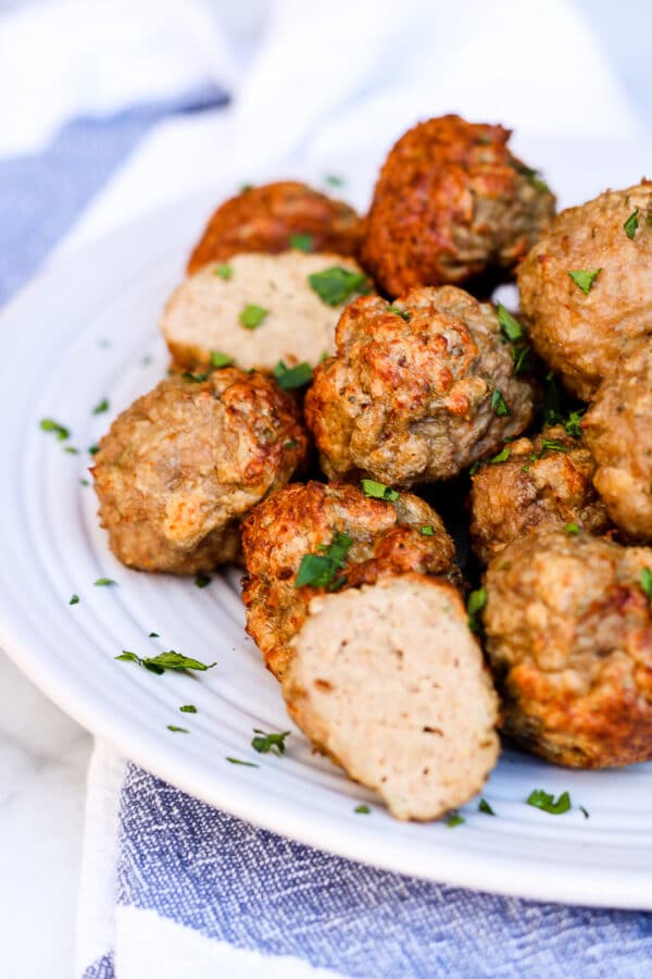 a plate of crispy meatballs garnished with fresh parsley, with one meatball cut open to exhibit juicy interior