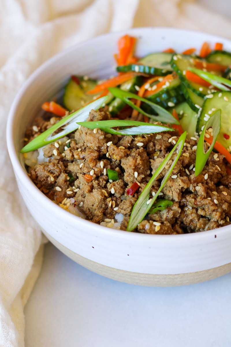 a stone bowl full of fluffy white rice, korean ground turkey, cucumber carrot salad, and garnished with sesame seeds and green onion