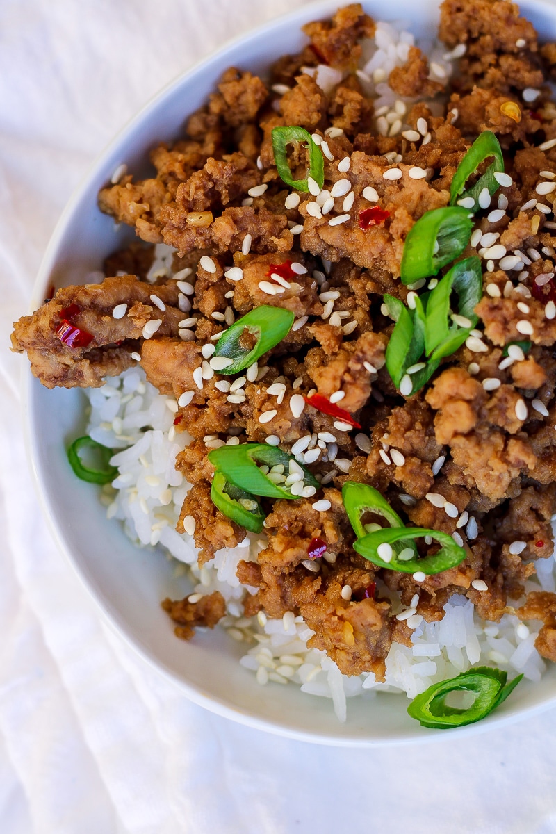 a bowl of white rice topped with saucy ground turkey, dotted with red chili flakes, green onions, and sesame seeds