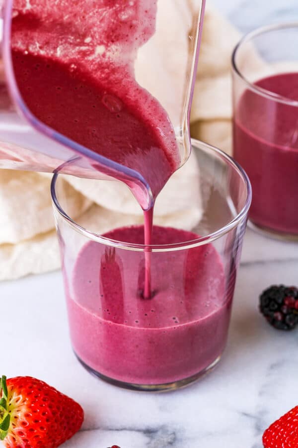 pouring a blackberry strawberry banana smoothie into a glass