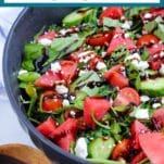 fresh salad topped with watermelon in a bowl with text overlay "watermelon basil salad"