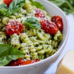a white bowl of pasta al pesto studded with blistered balsamic cherry tomatoes
