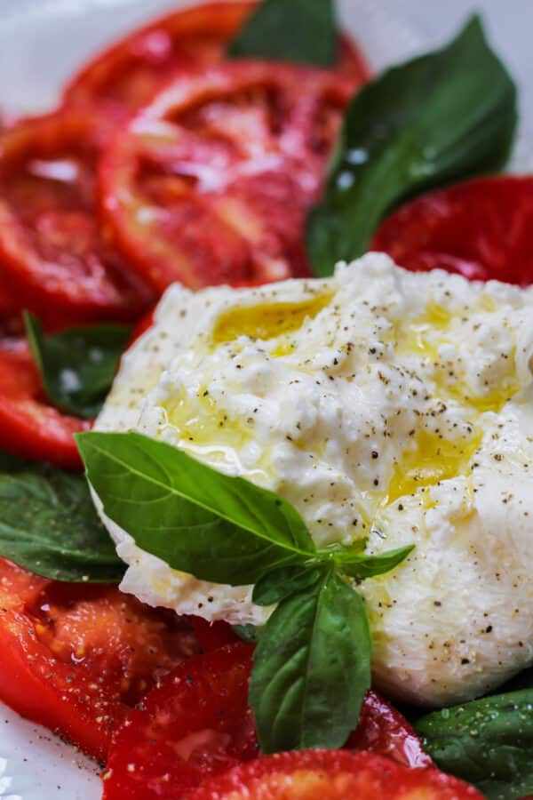 a ball of caprese drizzled with olive oil on a platter of tomato and basil caprese salad