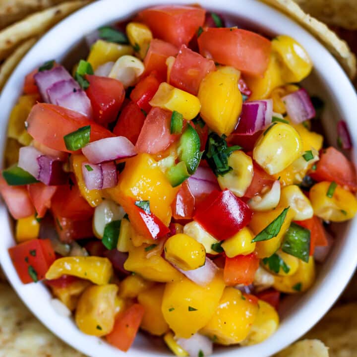 a close up of a bowl of mango corn salsa surrounded by tortilla chips