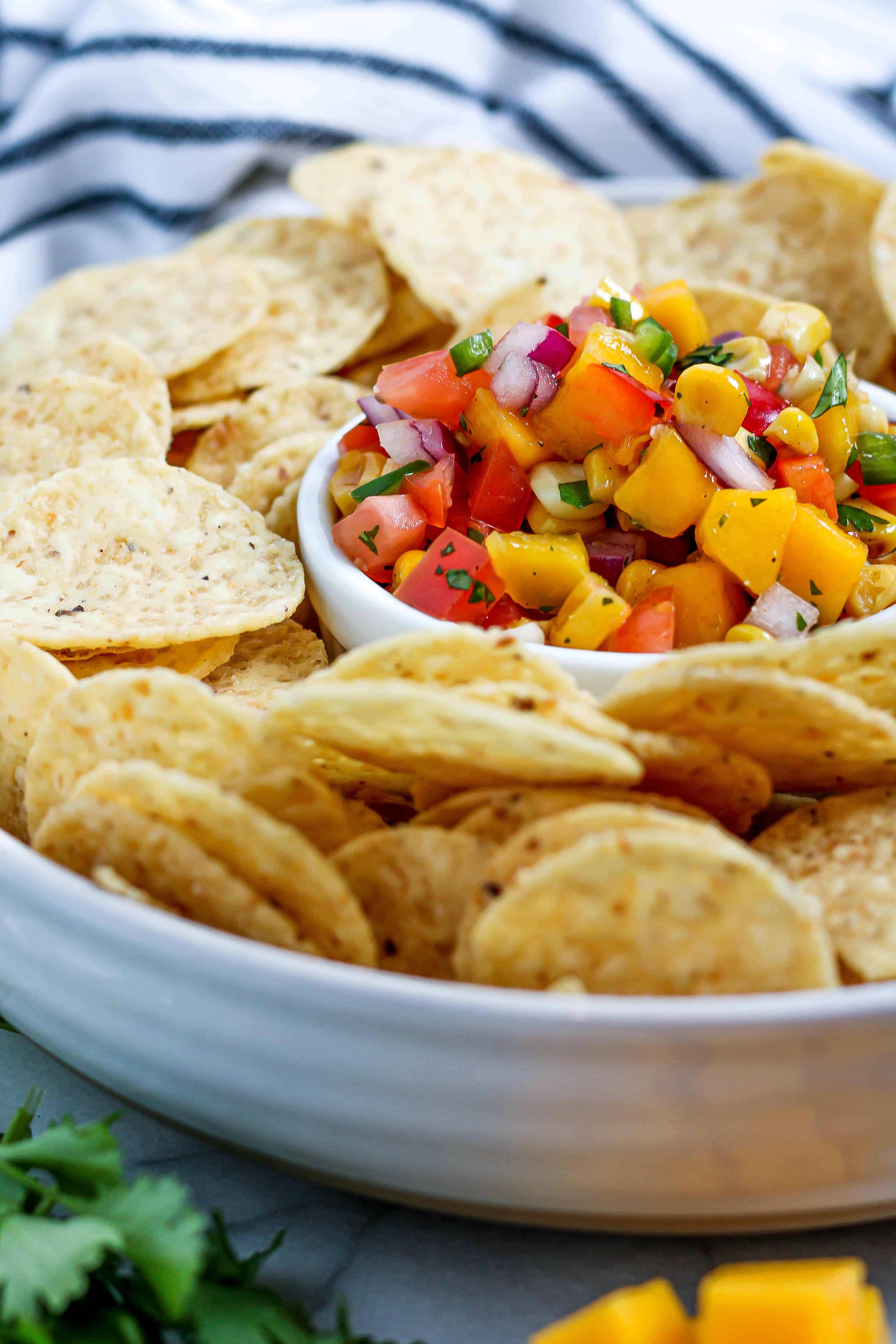 chips surrounding a dish of mango corn salsa