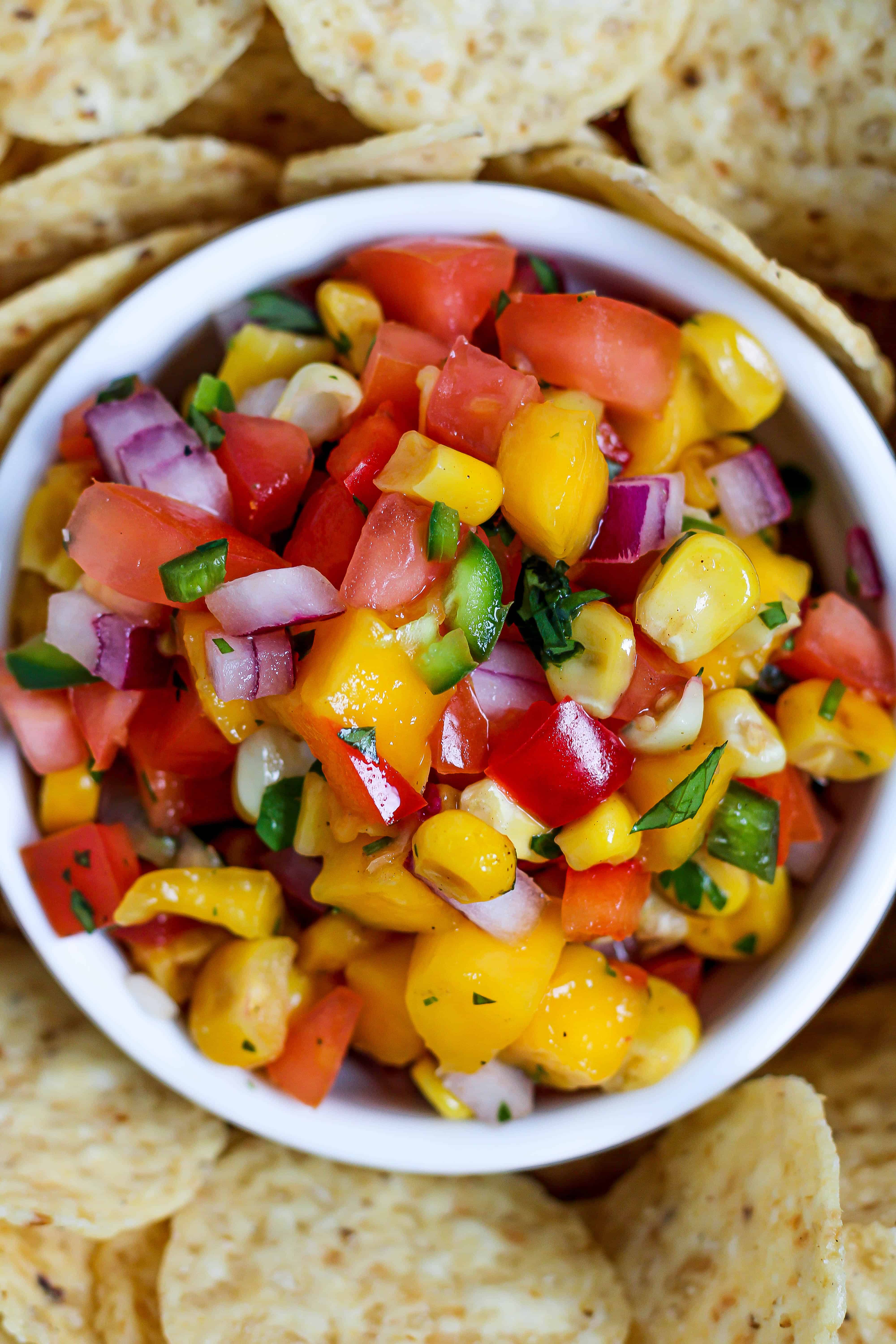 a close up of a bowl of mango corn salsa surrounded by tortilla chips