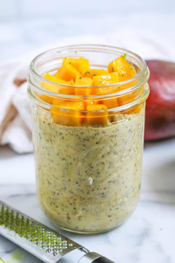 a jar of mango overnight oats topped with fresh mango and lime zest