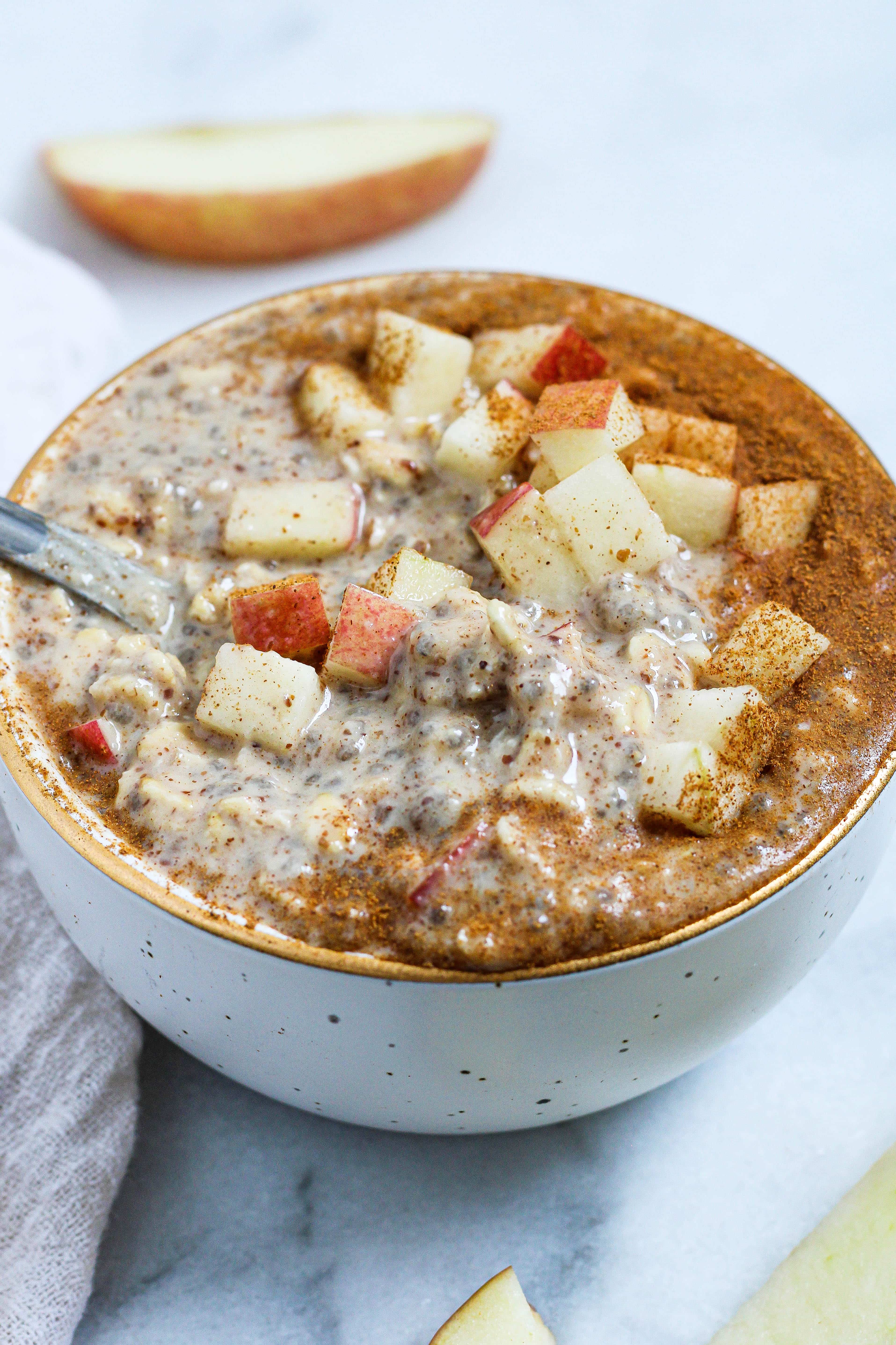 A spoon getting a bite of apple pie overnight oats out of a white bowl