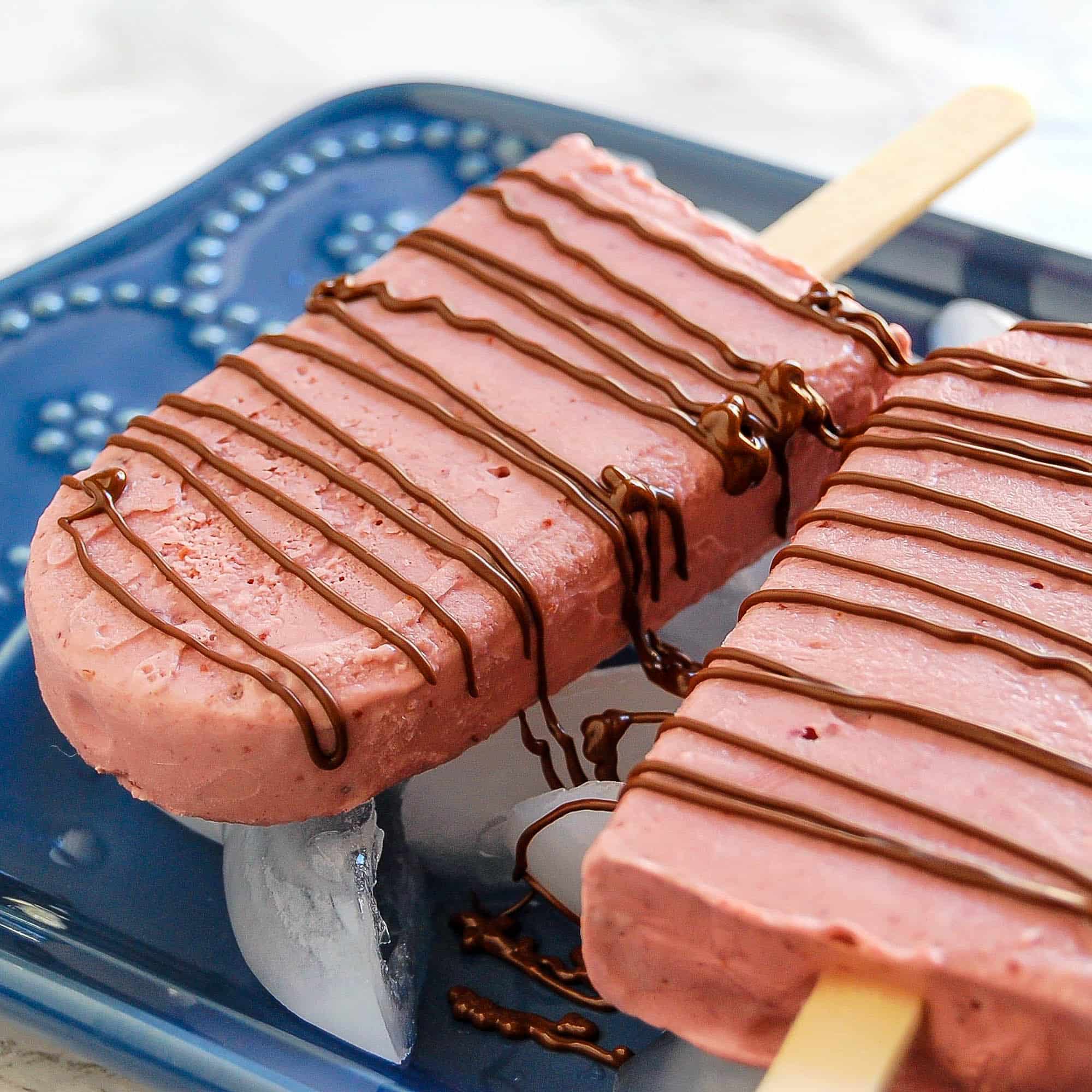 chocolate drizzled cherry popsicles on a blue platter with ice
