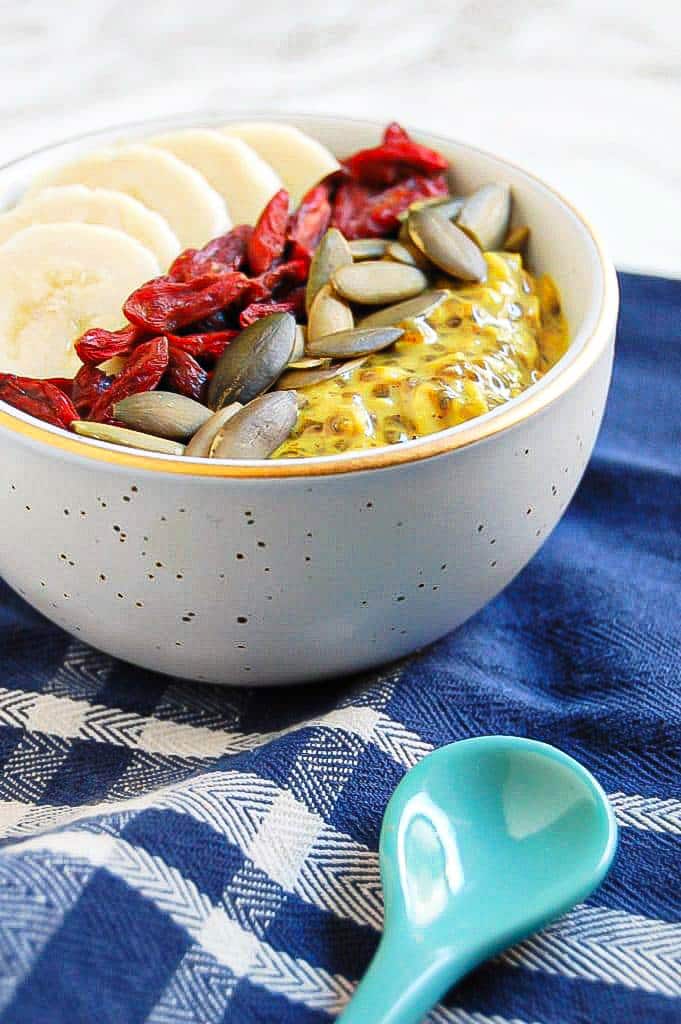 turmeric overnight oats in a white bowl topped with banana, pumpkin seeds, and goji berries
