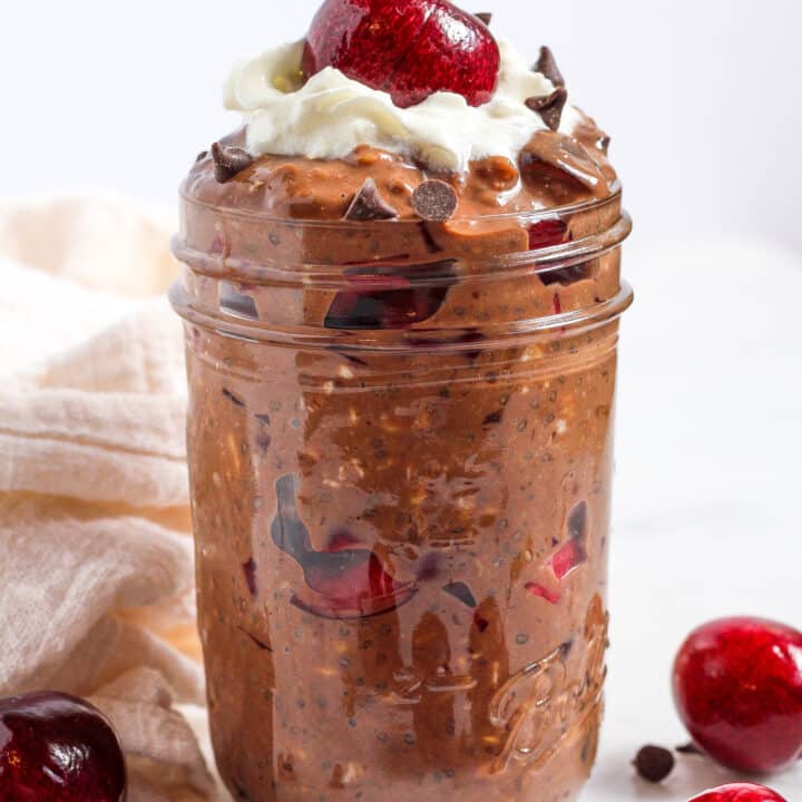 a cherry on top of a jar of chocolate cherry black forest overnight oats