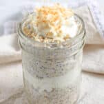 A jar of coconut cream pie overnight oats layered with whipped cream