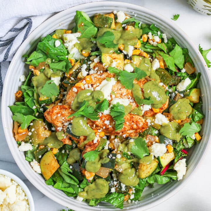 a bowl of poblano corn salad with chicken topped with avocado dressing, queso fresco, and cilantro