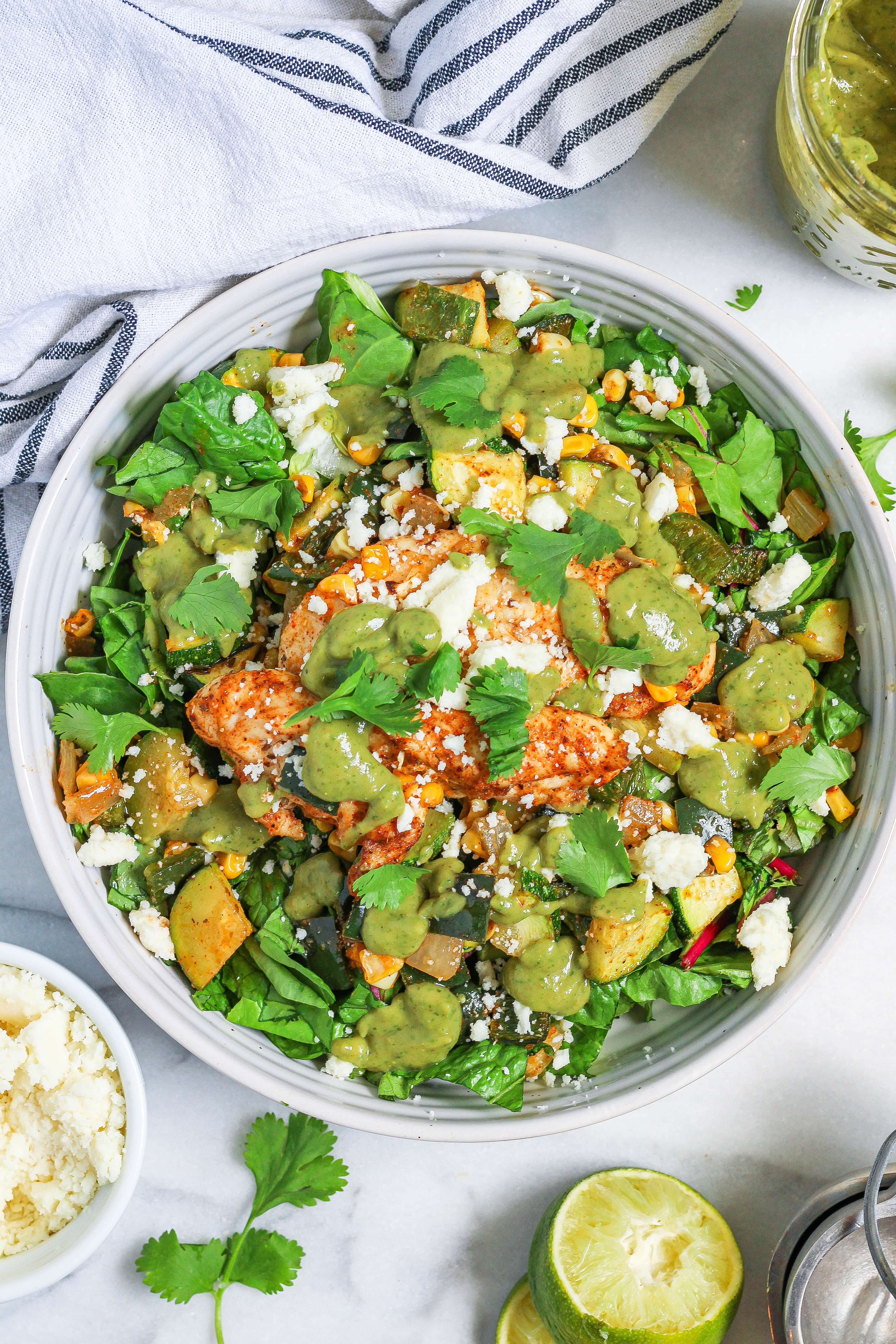 a bowl of poblano corn salad with chicken topped with avocado dressing, queso fresco, and cilantro