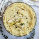 a bowl of asiago mashed potatoes topped with asiago cheese and thyme