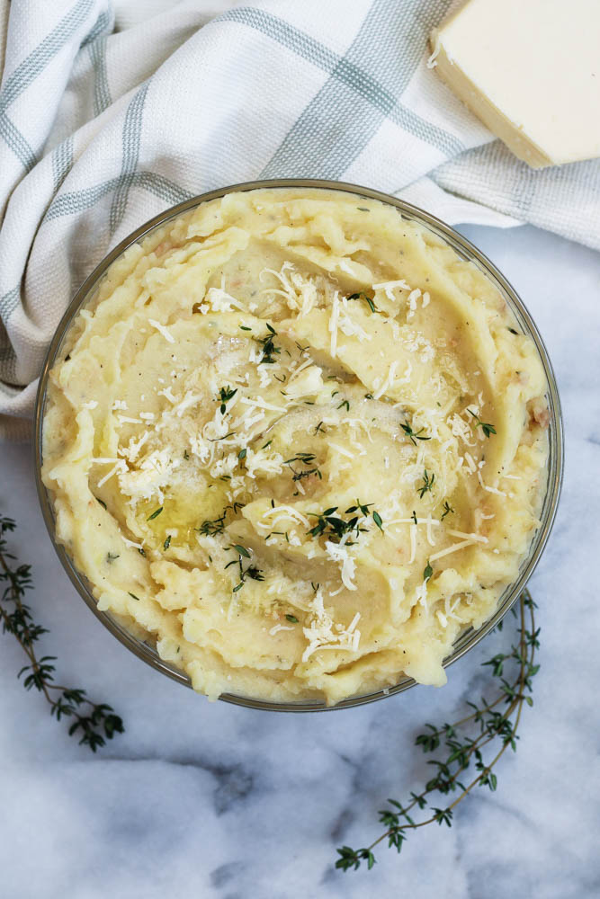 a bowl of asiago mashed potatoes topped with asiago cheese and thyme