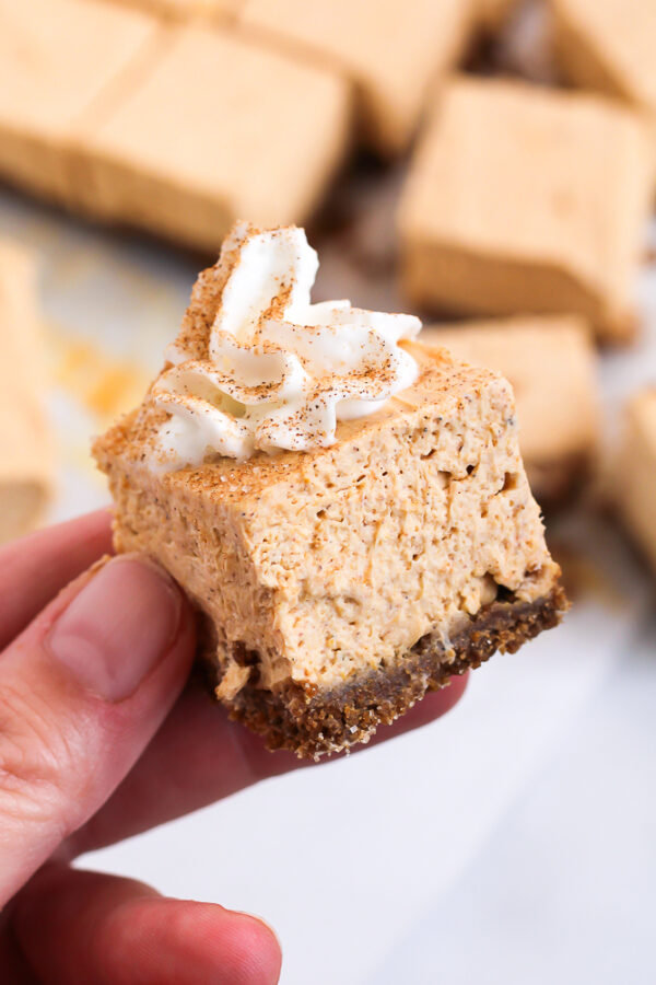 rich and creamy no bake pumpkin cheesecake bars with a gingersnap crust and whipped topping garnished with cinnamon sugar
