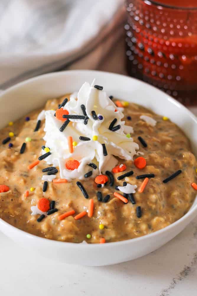 white bowl of pumpkin overnight oats with whipped cream and halloween sprinkles on top