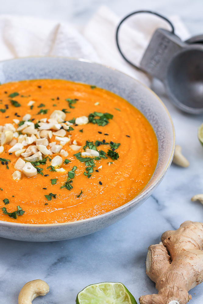 bowl of cashew carrot ginger soup garnished with cashews and cilantro