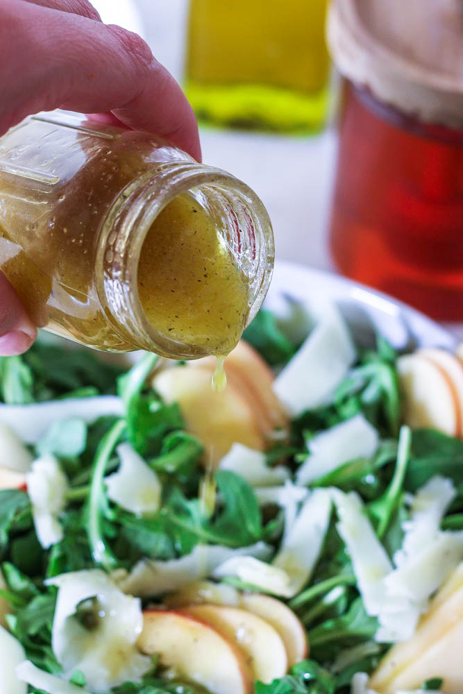 pouring apple cider vinaigrette over an apple manchego salad