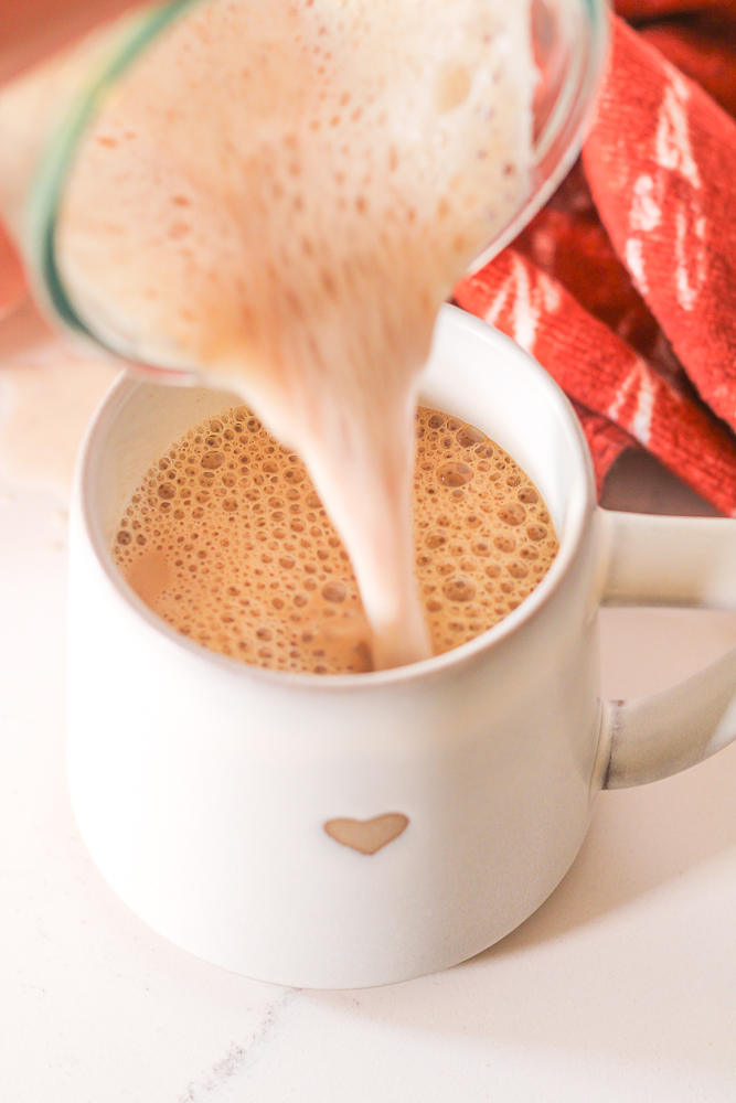 pouring steamed milk into a mug of espresso to make a honey cinnamon latte