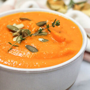 roasted carrot and butternut squash soup in a stoneware bowl with thyme and pumpkin seed garnish