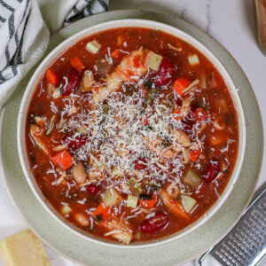 a bowl of chicken minestrone soup topped with grated parmesan