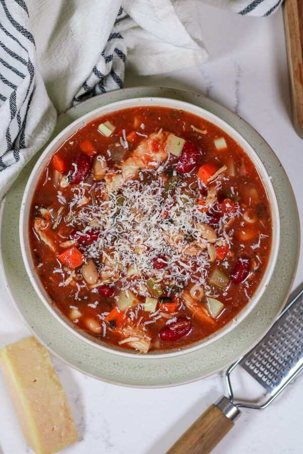 a bowl of chicken minestrone soup topped with grated parmesan
