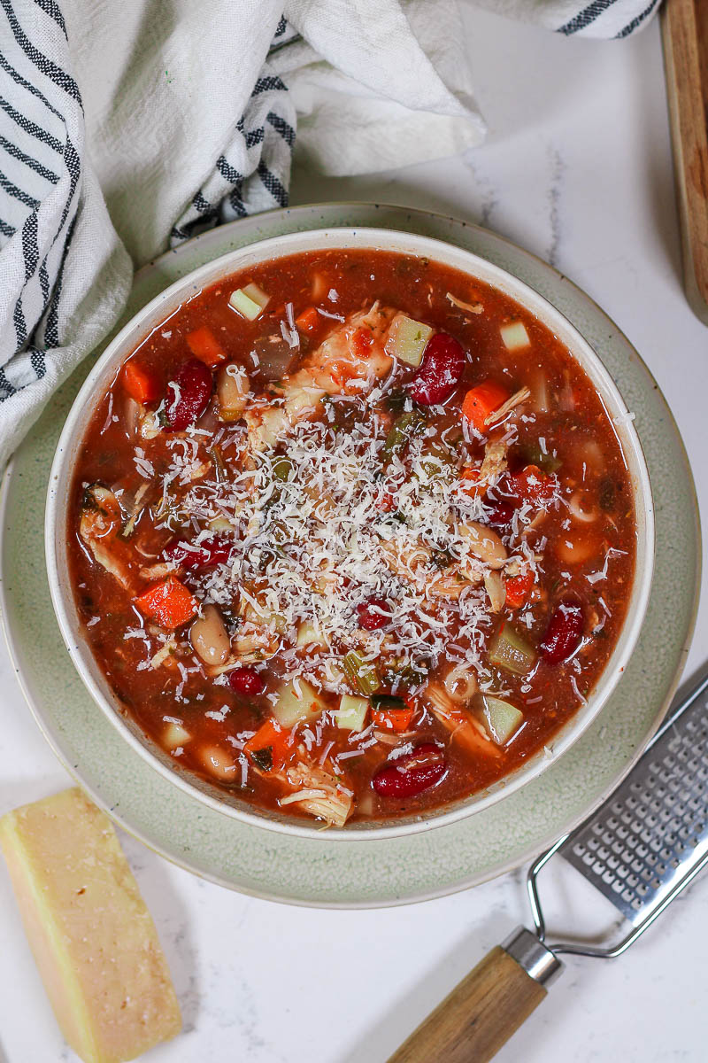 a bowl of chicken minestrone soup topped with grated parmesan