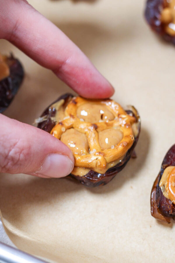 placing a pretzel on top of a peanut butter filled medjool date