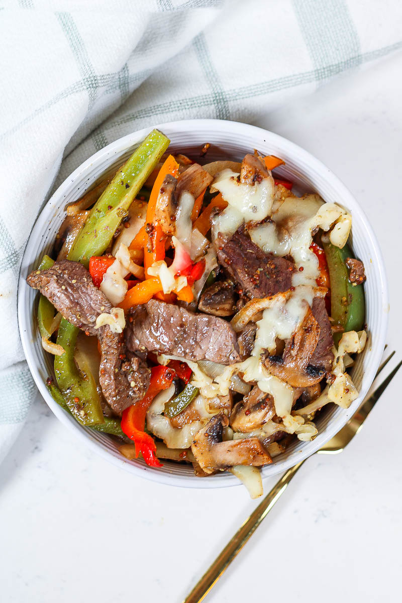 Philly Cheesesteak Bowls by a green kitchen towel and golden fork