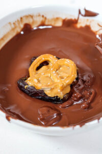 medjool date with peanut butter and pretzel being dipped in chocolate