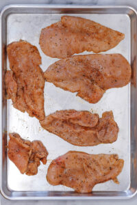 placing thin sliced chicken breasts on a sheet pan for meal prep
