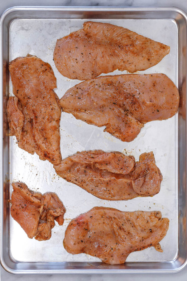 placing thin sliced chicken breasts on a sheet pan for meal prep