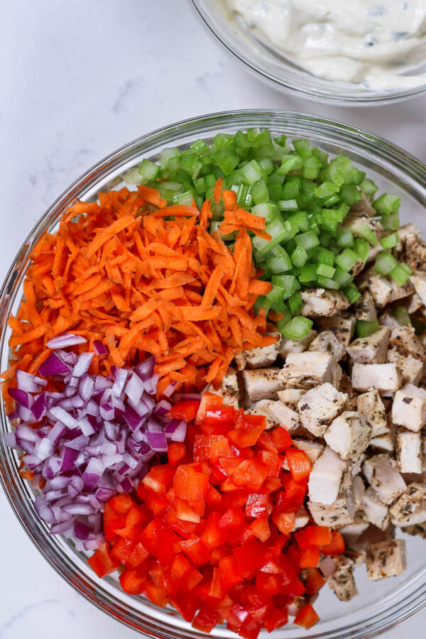 ingredients in a bowl next to a bowl of creamy dressing to make a healthier chicken macaroni pasta salad