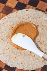 spreading peanut butter on a tortilla to make banana sushi