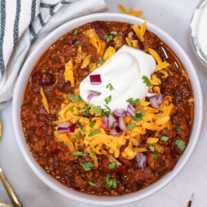 a bowl of pumpkin chili with turkey topped with greek yogurt, red onions, cheese, and cilantro