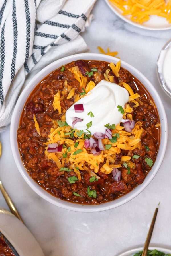 a bowl of pumpkin chili with turkey topped with greek yogurt, red onions, cheese, and cilantro