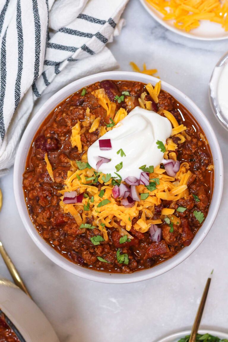 a bowl of pumpkin chili with turkey topped with greek yogurt, red onions, cheese, and cilantro