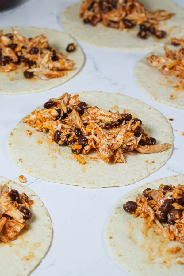 black bean chicken enchiladas filling on tortillas ready to be rolled up